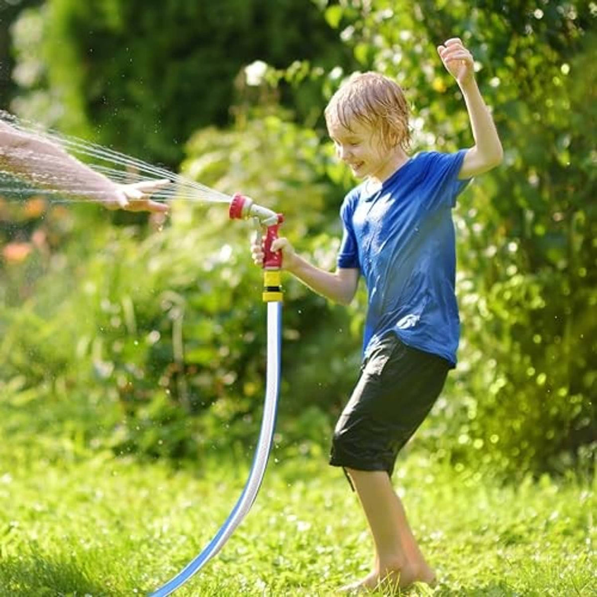 Child spraying water with a blue garden hose and nozzle