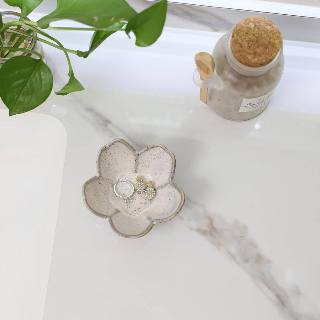 Ceramic flower jewelry dish on tabletop, holding a ring and pearl floral charm