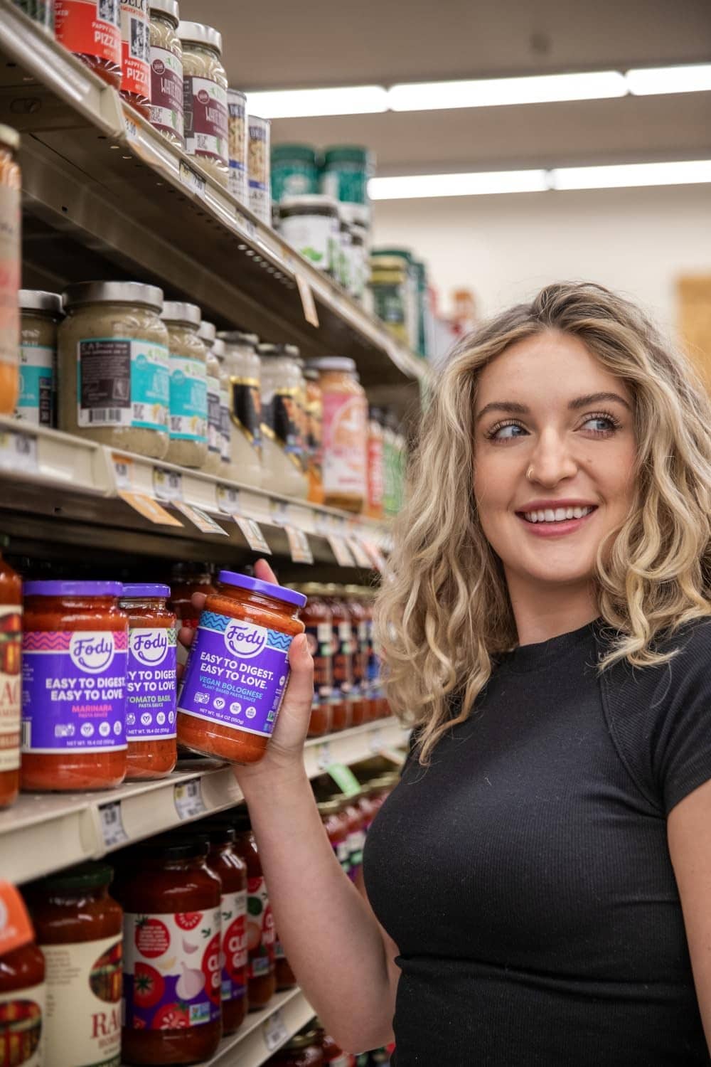 Fody tomato basil pasta sauce jars on a grocery shelf while shopper reaches