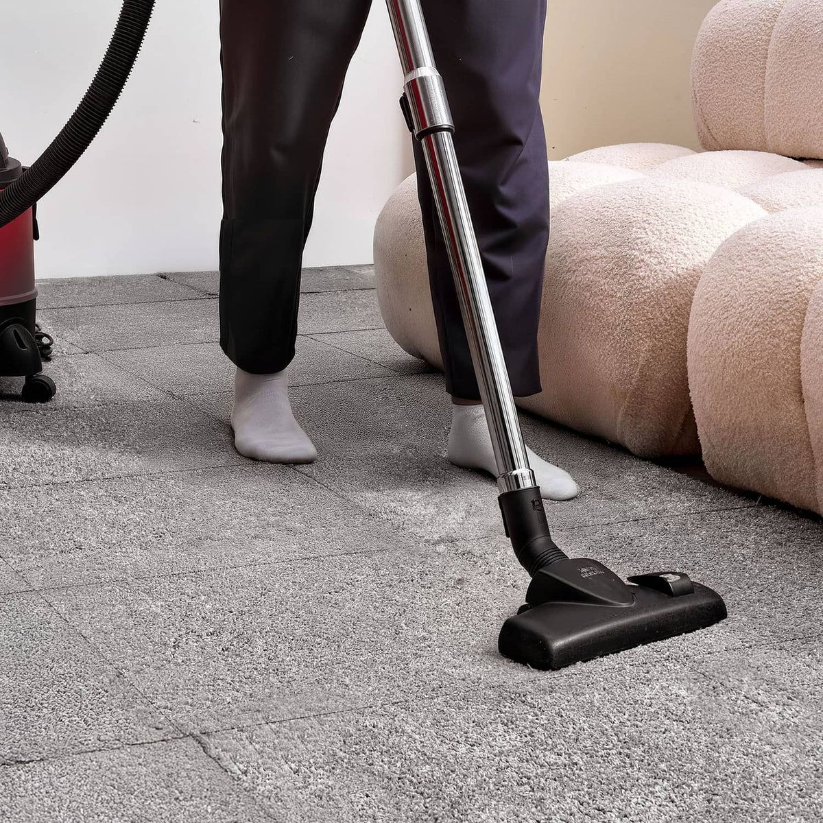 Vacuum cleaning a square carpet tile on the floor, showing low-pile texture