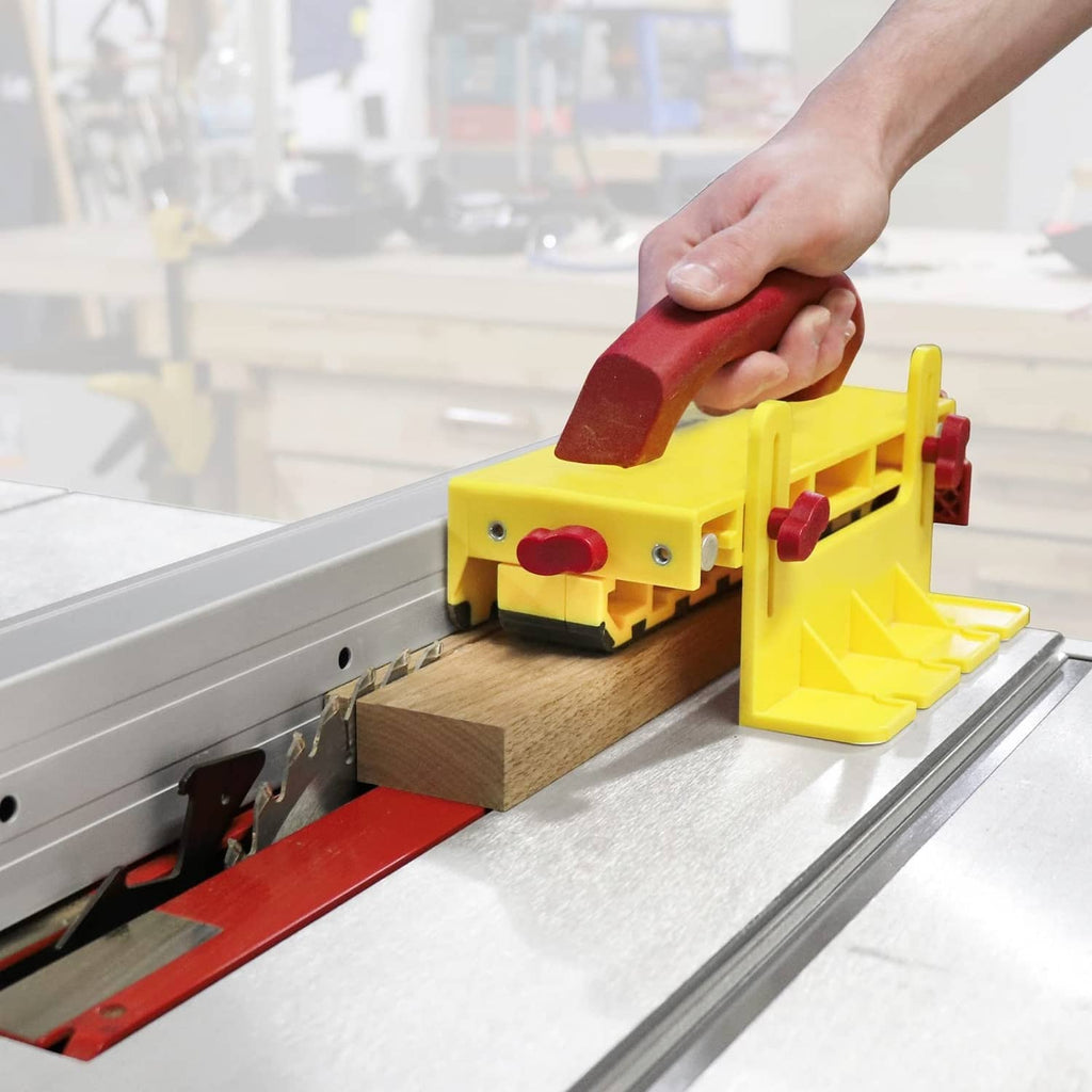 Yellow and maroon push block pressing a wooden board on a metal saw table