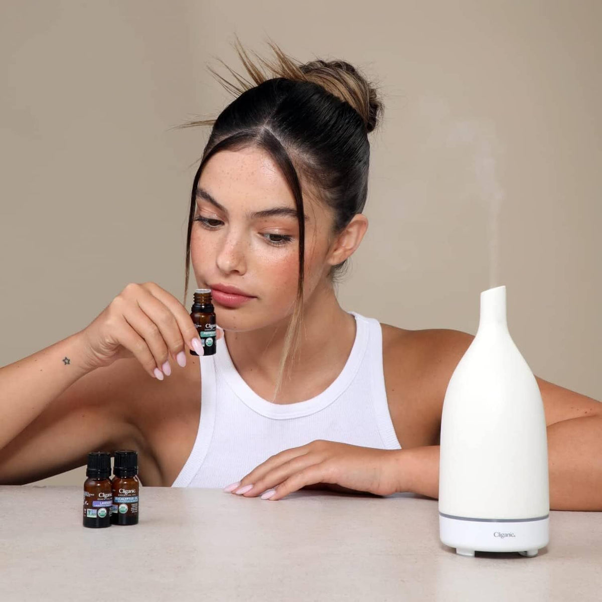 Lavender essential oil diffuser with amber bottles on tabletop, beside a woman.