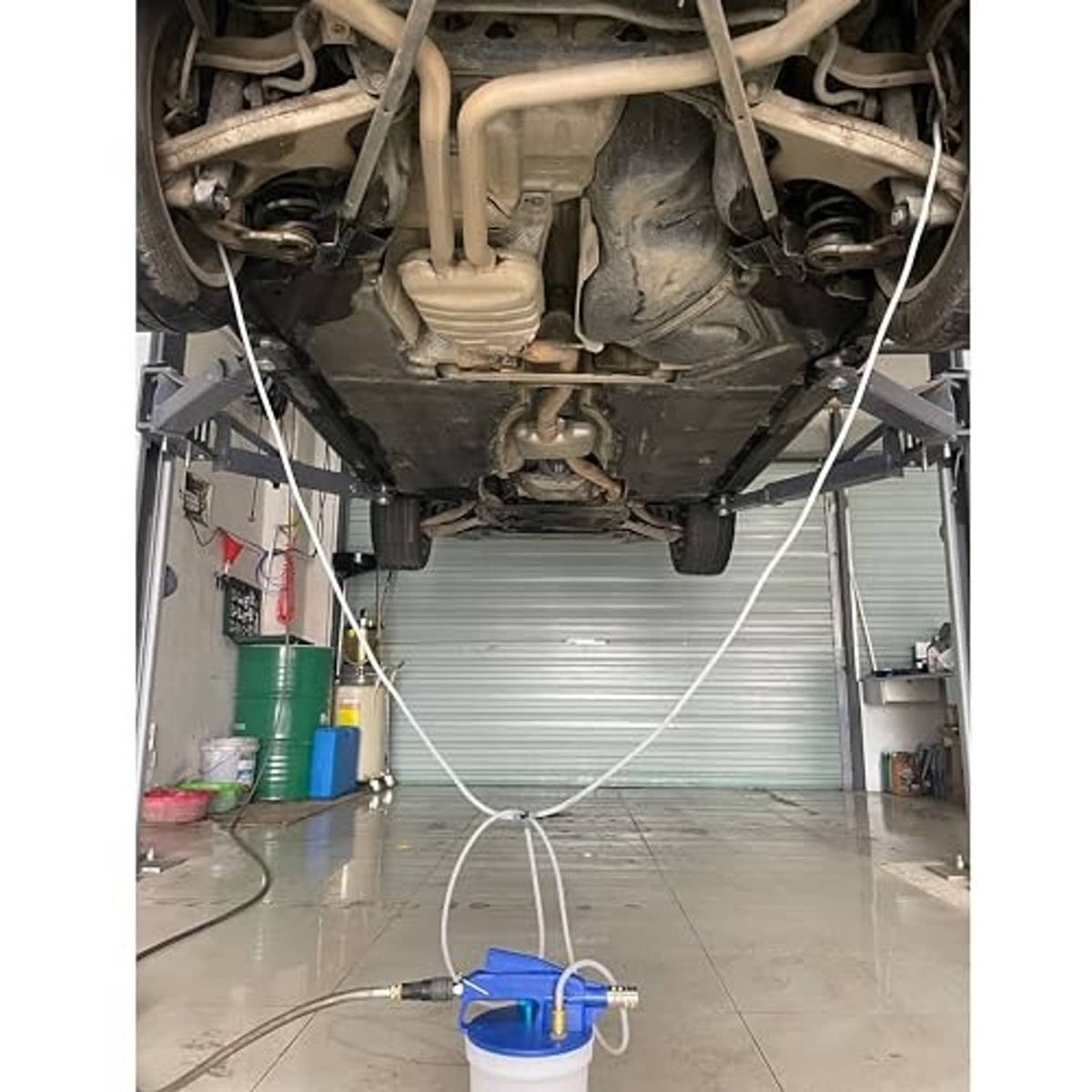 Vacuum brake bleeder setup in a garage with blue pump connected to car engine bay by hoses