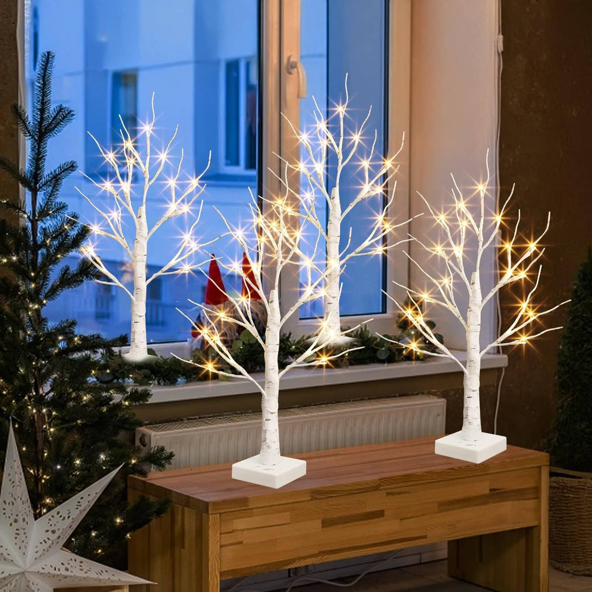 Lighted birch tree decorations with white trunks and warm LED lights by window