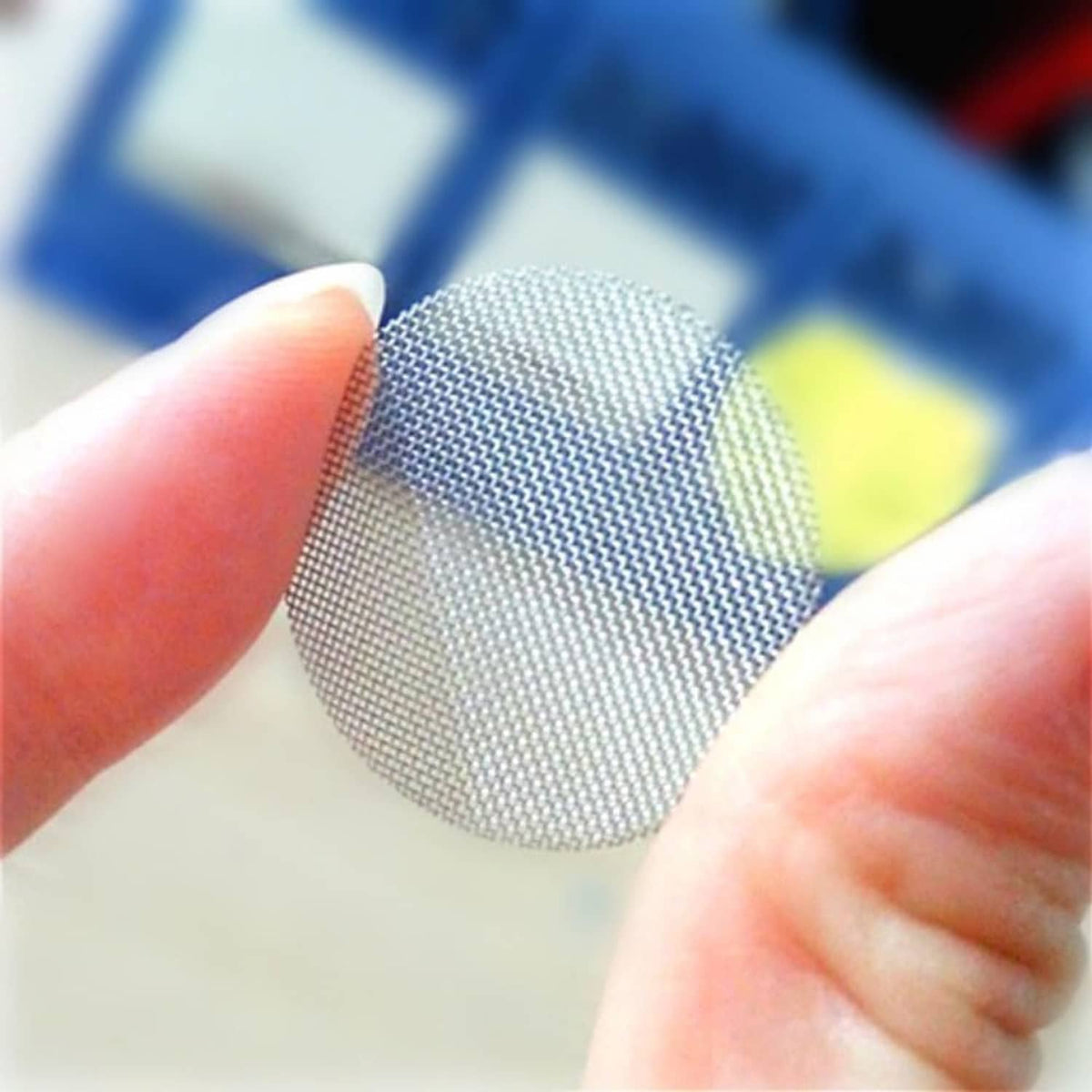 Stainless steel faucet screen mesh disc held between fingers, fine silver mesh