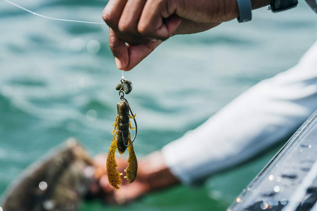 Hand holding lime green craw lure with dark spots over the water