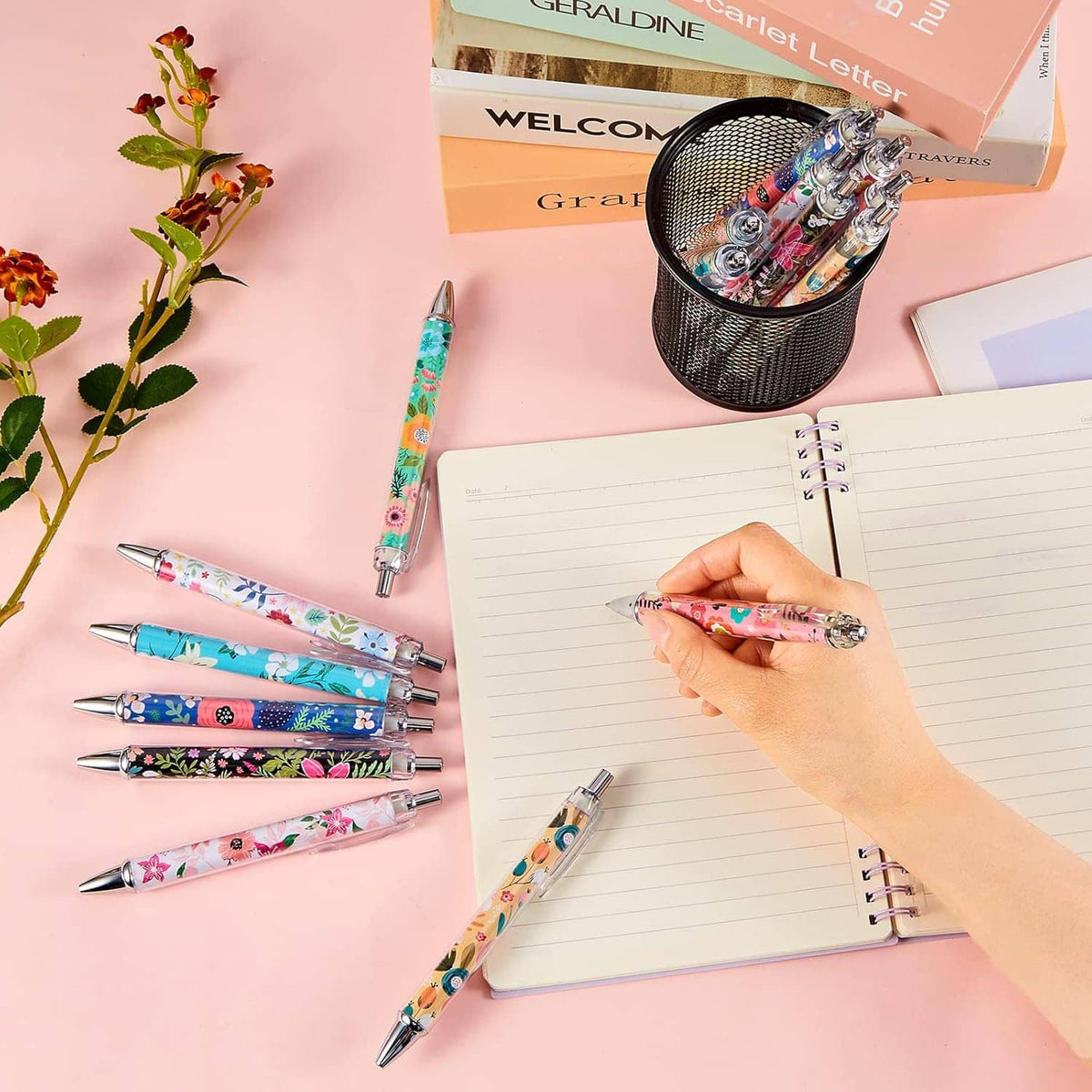 Floral ballpoint pens and notebook on a desk, one pen being used to write