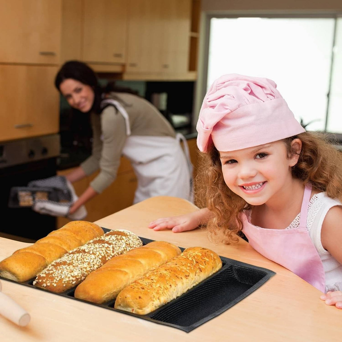 Black silicone hot dog mold with five baked rolls on a tray during baking