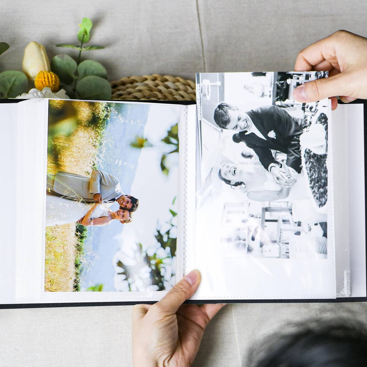 Black photo album open with two photos in pockets, hands turning pages
