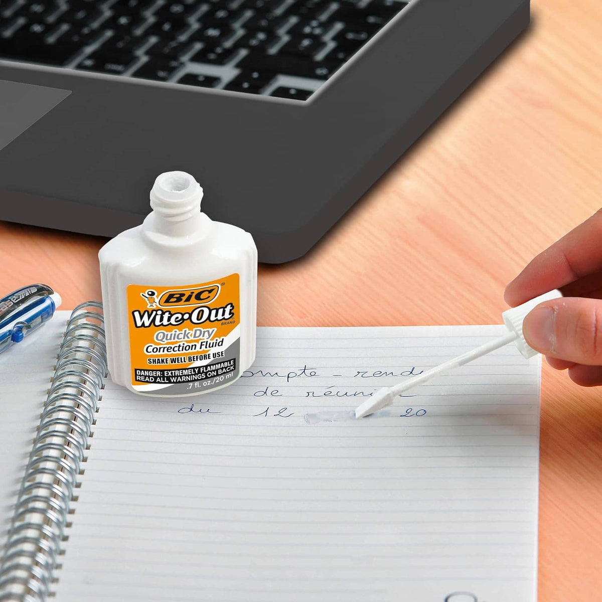 White correction fluid bottle with applicator over handwritten notes on desk