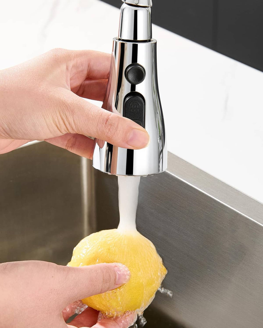 Hand holding chrome pull-down sprayer head over sink for rinsing
