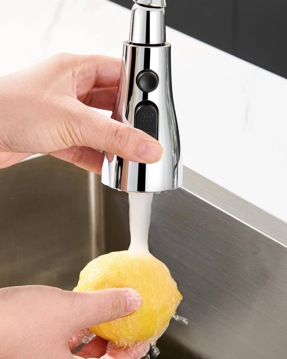 Hand holding chrome pull-down sprayer head over sink for rinsing