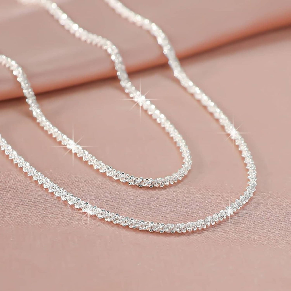 Close-up of layered silver-tone chain necklaces with tiny link sparkle