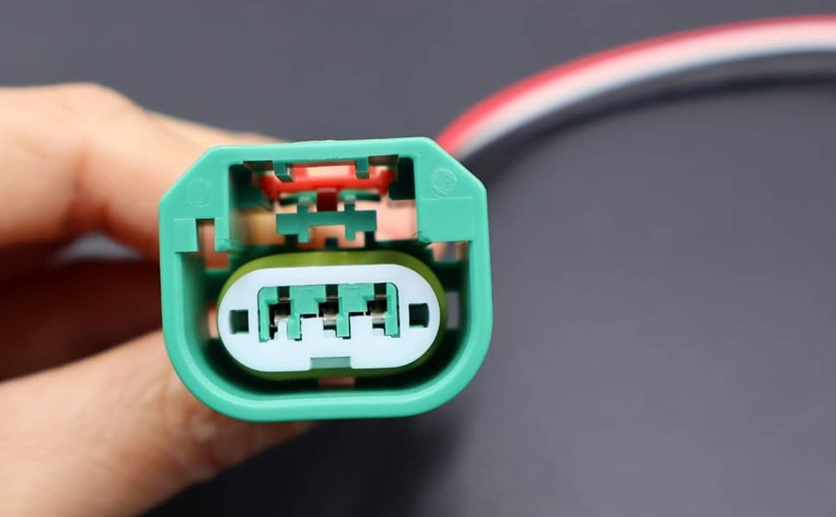 Green headlight connector socket close-up with internal contacts; hand holding it
