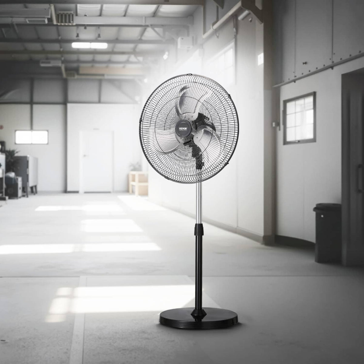 Black industrial pedestal fan with circular wire grille and tall stand in a workshop
